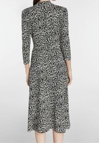 Czarna i biała sukienka z teksturowanym wzorem, z wydłużonymi półrękawami, dopasowanym korpusem i rozkloszowanym dołem.