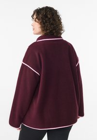 Burgundia fliisi jakk, millel on roosad aktsendid, omab mugavat lõike, pikki varrukaid ja kraed. Tekstuuriga kangas, kus on nähtavad õmblused.