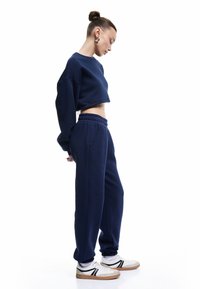 Marineblå sweatshirt med en cropped design, parret med matchende joggerbukser med elastisk talje og sidelommer. Hvide sneakers med sorte detaljer.