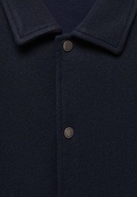 Navy wool blend jacket featuring a fold-over collar, button closure, and textured fabric. Subtle sheen and minimalistic design details.