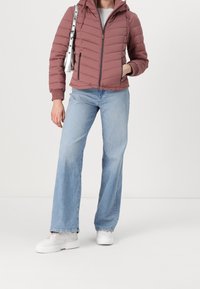 Jasnoróżowa kurtka puchowa z kapturem, zapinana na zamek z przodu, z bocznymi kieszeniami, w połączeniu z jasnoniebieskimi dzwonami i białymi trampkami. Srebrny detal torby.