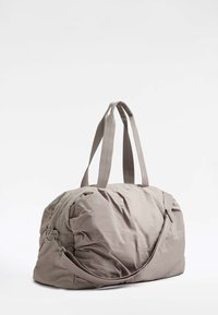 Harmaa nyloni-duffel-laukku, jossa on kaksi yläkahvaa, säädettävä olkahihna ja vetoketjukiinnitys. Laukussa on pehmeä, teksturoitu pinta sekä laskostetut yksityiskohdat.