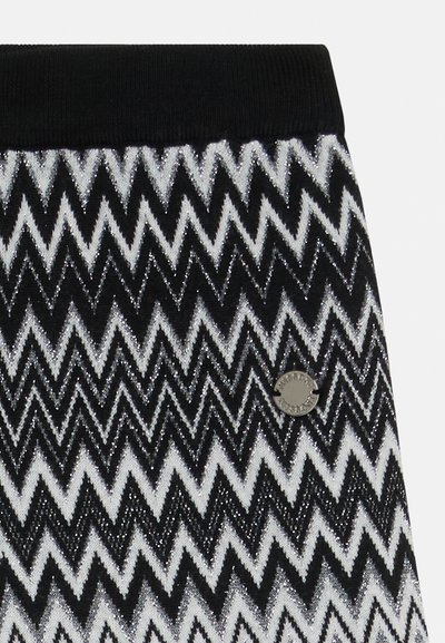 Svart och vitt tyg med zigzag-mönster och skimrande silverdetaljer. Har ett svart ribbat midjeband och en metalldetalj med logotyp.