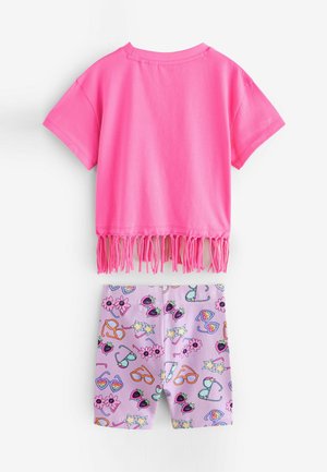 Tricou scurt roz cu detalii din franjuri și mâneci scurte, asortat cu pantaloni scurți lavandă care au modele colorate și jucăușe cu ochelari de soare și flori.