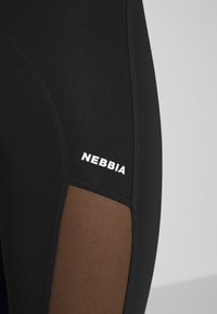 Fekete leggings hálós betétekkel barna színben, a fehér "NEBBIA" logóval. Simított textúra, testhezálló kialakítás. Varrott részletek jelenléte.