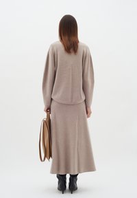 Šviesiai kreminės spalvos mezginys ir suderinta ilgų sijonų su laisvu siluetu. Lygus paviršius. Juodi aukštakulniai batai ir kreminės spalvos rankinė.