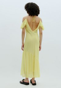 Geel maxi-jurk met ruffle-mouwen en een diepe V-hals. Beschikt over een vloeiende rok met een diagonale naad en een gestructureerde, lichte stof.