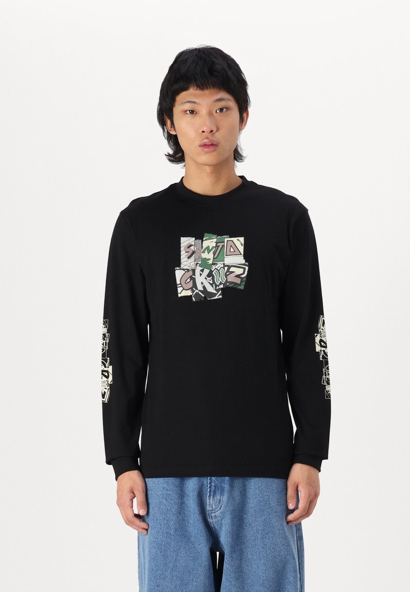 T-shirt noir à manches longues avec un design graphique sur le devant et les manches, présentant un texte coloré et un motif camouflage. Porté avec un jean bleu clair.