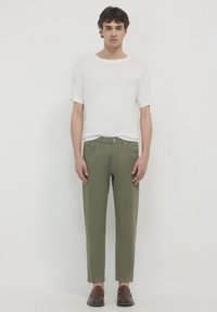Pantaloni in cotone verde con una vestibilità affusolata, abbinati a una maglietta bianca a maniche corte con collo tondo. Mocassini marroni completano l'outfit.