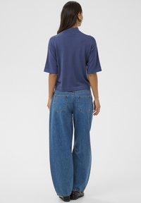 Tengerészkék, rövid ujjú, galléros felső, laza fazonú kék farmernadrággal párosítva. A farmeren két hátsó zseb látható.