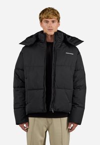 Črna puffer jakna z visokim ovratnikom, zadrgo in quilted oblikovanjem. Narejena iz gladkega materiala, z logotipom na prsih.