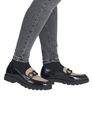 Black patent leather shoes with a beige suede panel and decorative black hardware. Thick, textured black rubber soles. Worn with gray jeans.