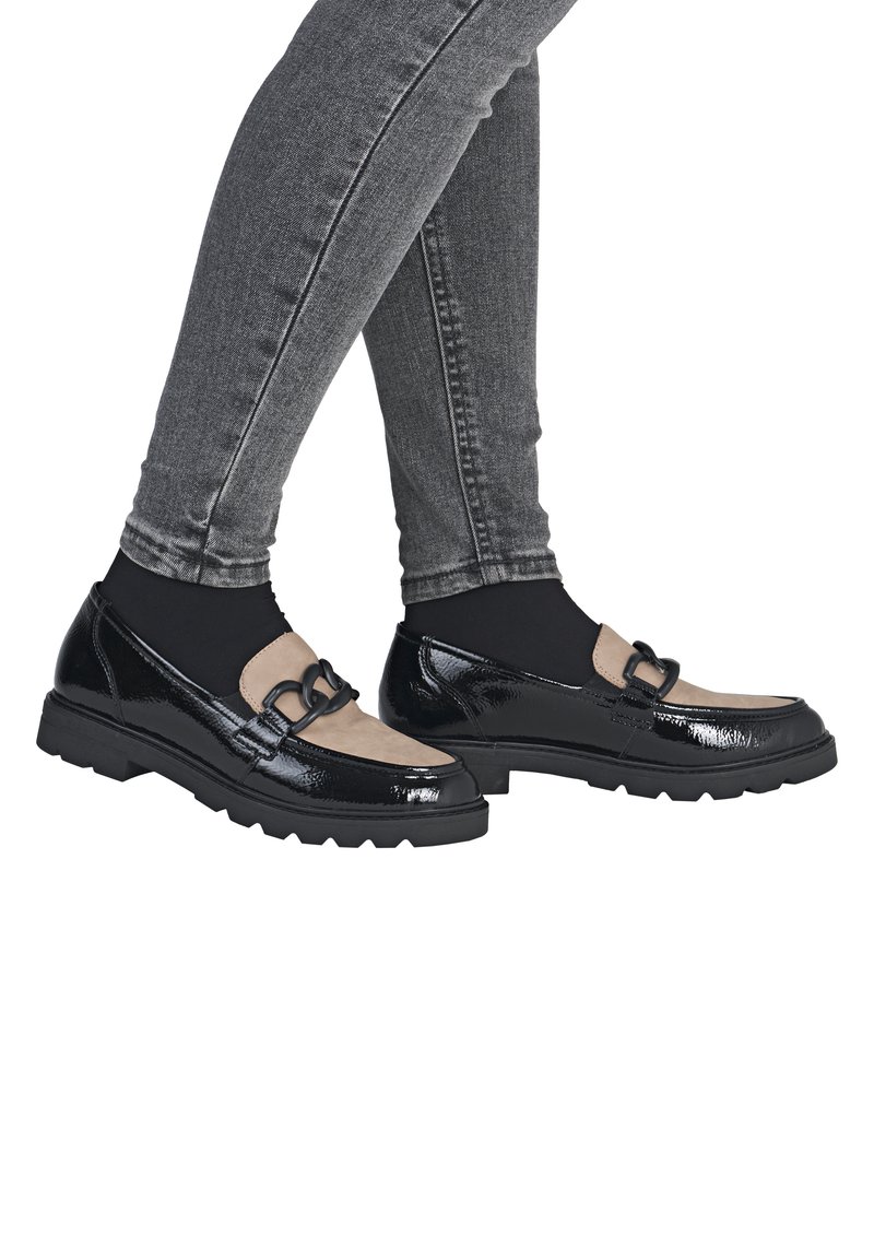 Black patent leather shoes with a beige suede panel and decorative black hardware. Thick, textured black rubber soles. Worn with gray jeans.