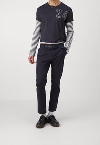 Marinblå kortärmad skjorta med nummer "24" och randiga långärmar, i kombination med marinblå byxor och svarta skor. Bältet har flera hål.