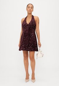 Vestido burdeos de tirantes con lentejuelas, cuerpo ajustado y falda acampanada. Llevado con un minibolso blanco. Textura suave y detalles brillantes.