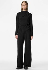 Melns tops ar garām piedurknēm un drapētu kakla izgriezumu, kombinēts ar teksturētām platām biksēm. Abiem apģērbiem ir viendabīga krāsa un moderna siluets.