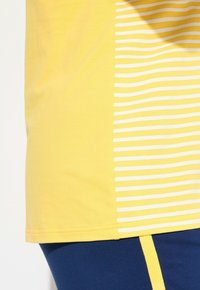 Gul kortärmad skjorta med vertikala vita ränder och en solid färg. Har mjukt bomullstyg och en avslappnad passform.