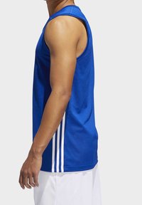 Man som bär en blå ärmlös atletisk tröja med vita ränder på sidan och vita shorts, visad från sidan av överkroppen ner.