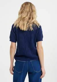 Maglietta a maniche corte in maglia blu navy con motivo texture. Presenta un orlo e polsini a costine, abbinata a jeans blu a vita alta.