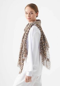 Leopardprint sjaal van lichtgewicht stof, met een zachte textuur, franjes aan de randen en tinten bruin en beige, gedragen over een witte top.