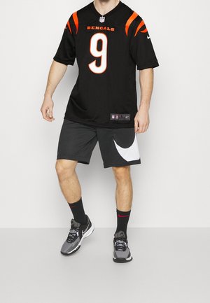 Schwarzes NFL Bengals-Trikot mit orangen Akzenten und der Nummer 9. Kombiniert mit grauen Shorts, die ein weißes Nike-Logo haben, und schwarzen Sportschuhen.