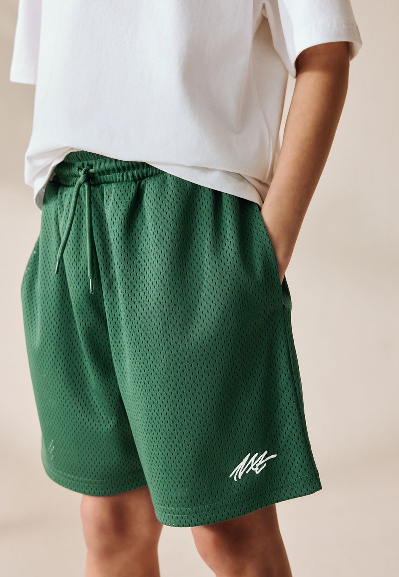 Grüne Mesh-Shorts mit atmungsaktiver Textur, ausgestattet mit einem elastischen Bund und Seitentaschen. Auffälliges weißes Markenlogo am unteren Bein.
