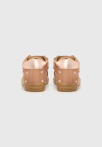 Rosa-goldene Sneakers mit glatten metallischen Akzenten und rosa Herzmustern an der Seite. Besitzen eine strukturierte beige Sohle. Retro, niedrige Silhouette.