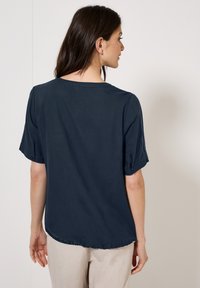 Blusa corta blu navy a maniche corte con scollatura tonda, dotata di maniche arrotolabili e orlo curvo, realizzata in un tessuto leggero e morbido.