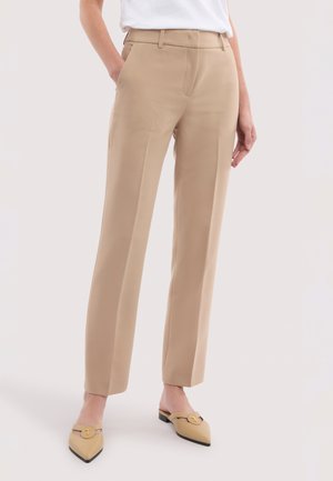 Beige op maat gemaakte recht gesneden broek gedragen met beige puntige instapschoenen, gecombineerd met een wit ingestopt shirt.