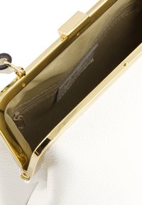 Innenansicht einer weißen Lederhandtasche mit goldfarbenem Metallrahmen, beigem Stofffutter, Reißverschlusstasche und glatter Textur. Sichtbarer Verschluss.