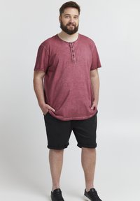 Korte ermer maroon T-skjorte med rund hals og tre-knappløsning, sammen med svarte rullede shorts og svarte joggesko.
