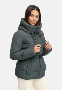 Tumši zaļš puffers jaka ar augstu apkakli, regulējamiem aukliņām, priekšējo rāvējslēdzēju un jostu viduklī. Iezīmējas ar quilted tekstūru un divām sānu kabatām.