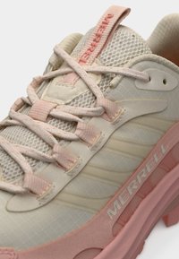 Chaussure de sport beige clair avec empeigne en mesh et accents roses. Présente des détails texturés, un système de laçage central et un logo de marque sur le côté.