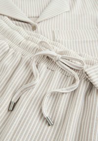 Ensemble de pyjama beige clair avec fines rayures verticales, chemise boutonnée à col, et taille élastique avec cordon de serrage et détails métalliques.