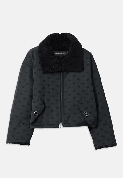 Čierna skrátená bunda s textúrovaným vzorom, vybavená huňatým čiernym golierom, bočnými vreckami a striebornými kovovými akcentmi. Zapínanie na zips.