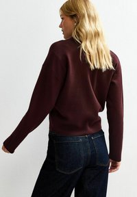 Burgundy knit sweater with long sleeves, a relaxed fit, and ribbed hem, paired with dark blue jeans featuring back pockets.