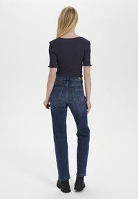 Top blu navy a coste con maniche corte, abbinato a jeans in denim blu scuro a vita alta con gamba affusolata e tasche posteriori. Stivaletti neri alla caviglia.