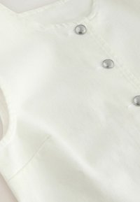 Close-up of white fabric with diagonal seam and three silver snap buttons on a garment.