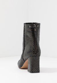 Botín de tobillo de imitación de piel de serpiente negra con tacón bloque, cremallera lateral y patrón texturizado. Forro interior suave y diseño de punta redonda.