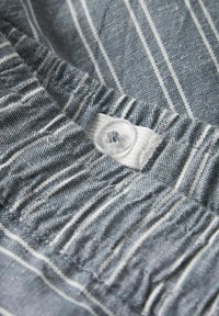 Tissu rayé dans des tons de bleu et blanc, présentant une couture froncée et un bouton transparent cousu sur une patte blanche.