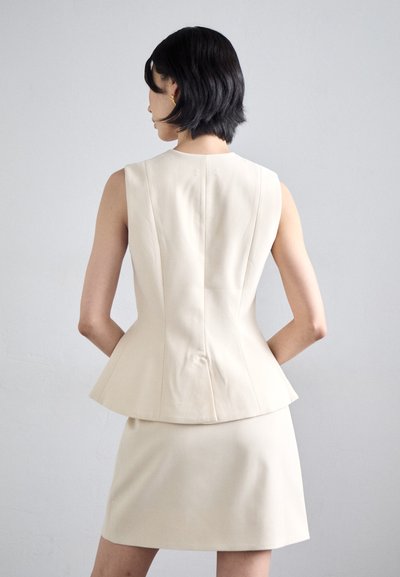 Beige peplum top med ærmeløs design og struktureret silhuet, parret med en matchende tætsiddende nederdel. Glat tekstur, minimal hardware.