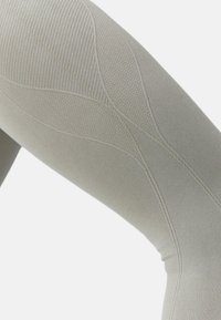 Šviesiai pilkos legging'os iš tekstūruoto audinio, su briaunotais raštais ir lygiais skyrių, matomais siūlių detalėmis ir formos kontūrais.