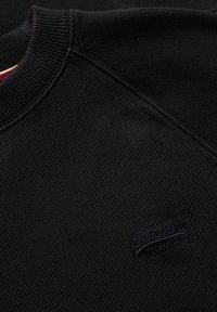 Felpa nera con texture a coste, collo rotondo e un logo ricamato in viola scuro sul lato sinistro del petto.