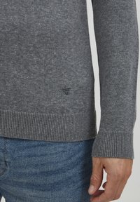Grå striktrøje med ribkant i bunden og ved ærmerne. Har et lille trekantet logo på nederste kant. Kombinationen er med blå denim jeans.