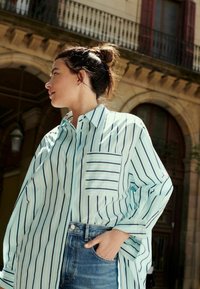 Lyseblå stribet oversized skjorte med en brystlomme, parret med højtaljede denimshorts. Blødt stof og afslappet pasform.