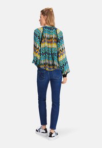 Multicolored long-sleeve blouse with vibrant zigzag pattern, paired with fitted blue jeans and black and white sneakers.