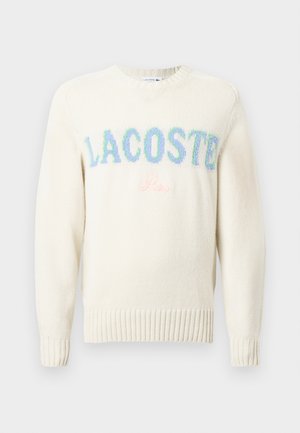 Krémový svetr s ribováním na rukávech a spodním lemu. Obsahuje mnohobarevně vyšívané loga "LACOSTE" a "Paříž" v jemných pastelových odstínech.