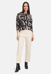 Black and cream patterned top with long sleeves, paired with light beige straight-leg pants and black heeled ankle boots.