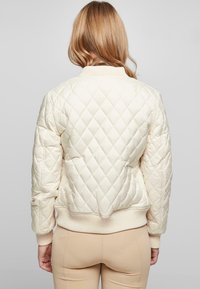 Chaqueta bomber de crema acolchada con puños y dobladillo acanalados, que presenta un diseño ajustado y un patrón de diamantes para añadir textura.
