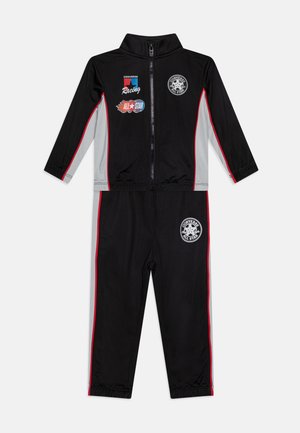 Čierny teplákový súprava s šedými akcentmi a červenými bočnými pruhmi. Obsahuje zips vpredu, vysoký golier a logo "Converse All Star" na hrudi.